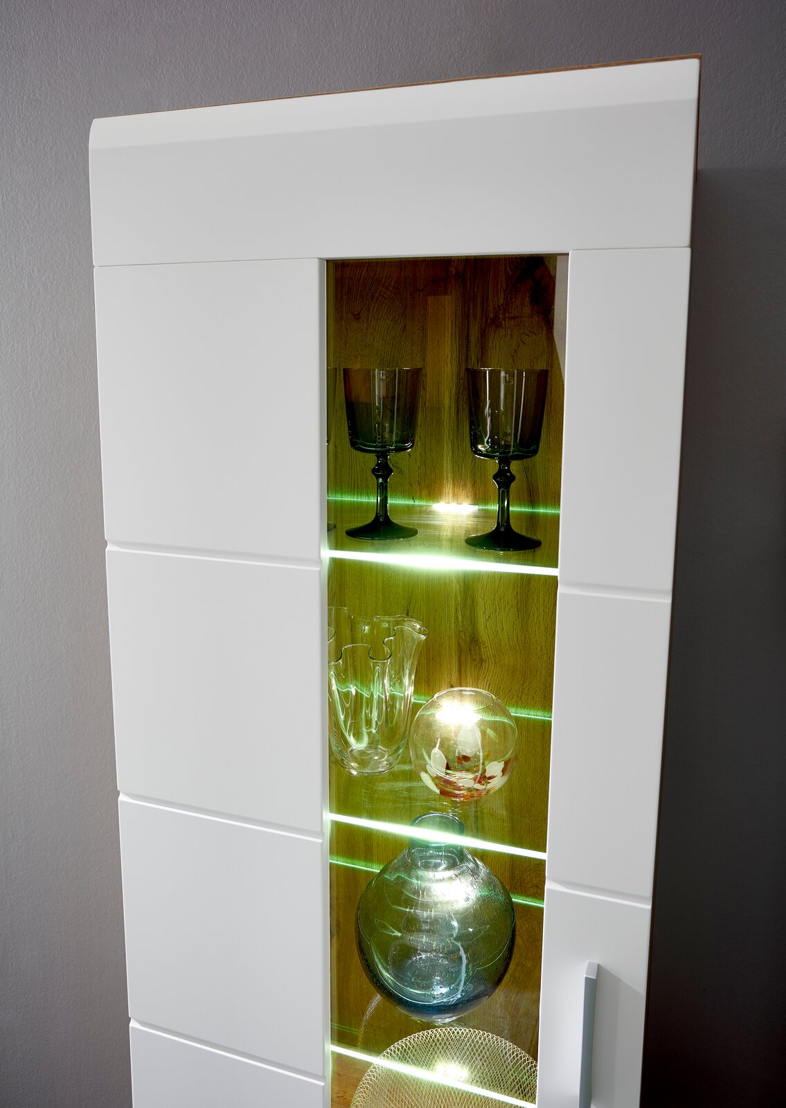 Detailansicht einer modernen Wandkombination mit Glastüren und LED-Beleuchtung, die Gläser und Dekorationsobjekte präsentiert.