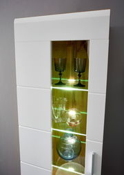 Detailansicht einer modernen Wandkombination mit Glastüren und LED-Beleuchtung, die Gläser und Dekorationsobjekte präsentiert.