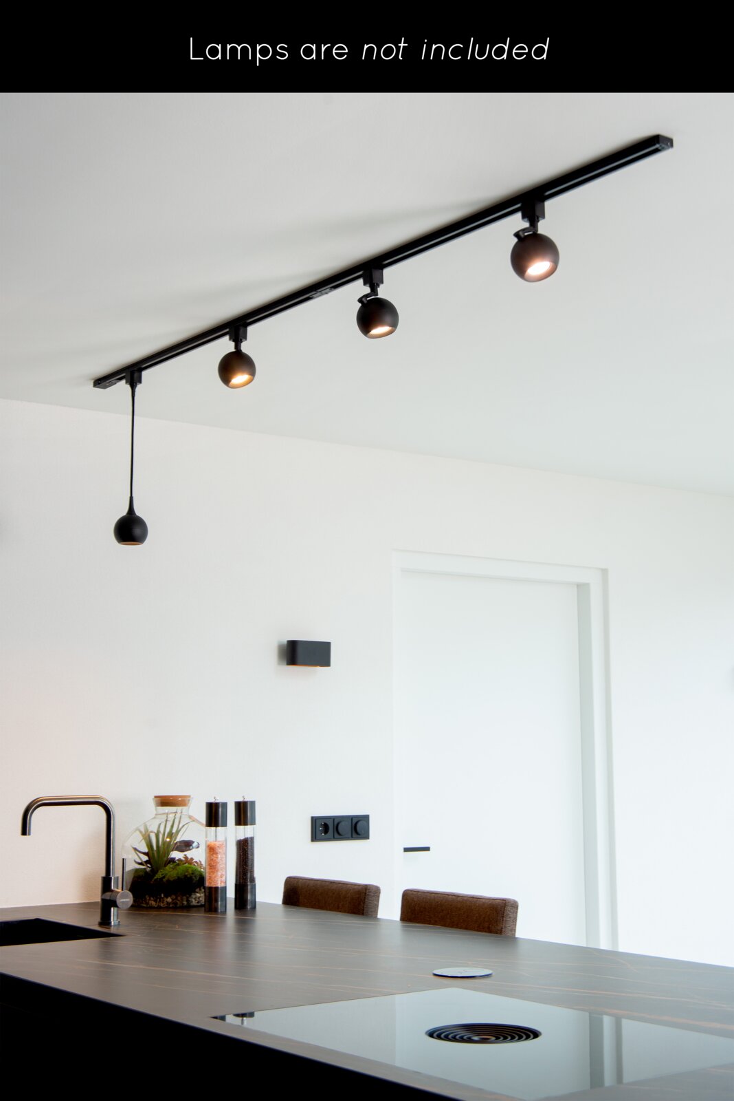 Een aan het plafond bevestigd railsysteem met drie zwarte spotjes in een moderne keuken, gezien van onderaf.