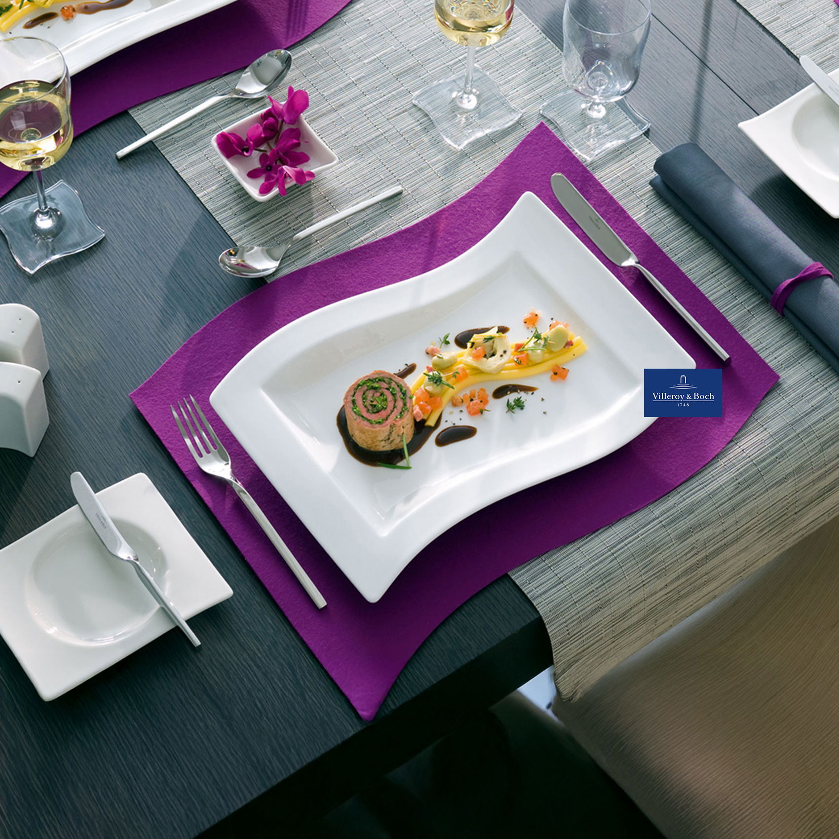 Elegant gedeckter Tisch mit modernem, geschwungenem Teller und feinem Gourmetgericht auf violettem Platzset