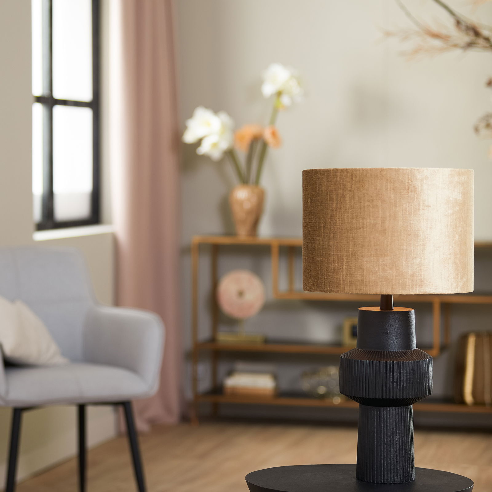 Moderner Lampenschirm Zylinder in Beige auf schwarzem Sockel, seitliche Perspektive in stilvollem Wohnzimmer.