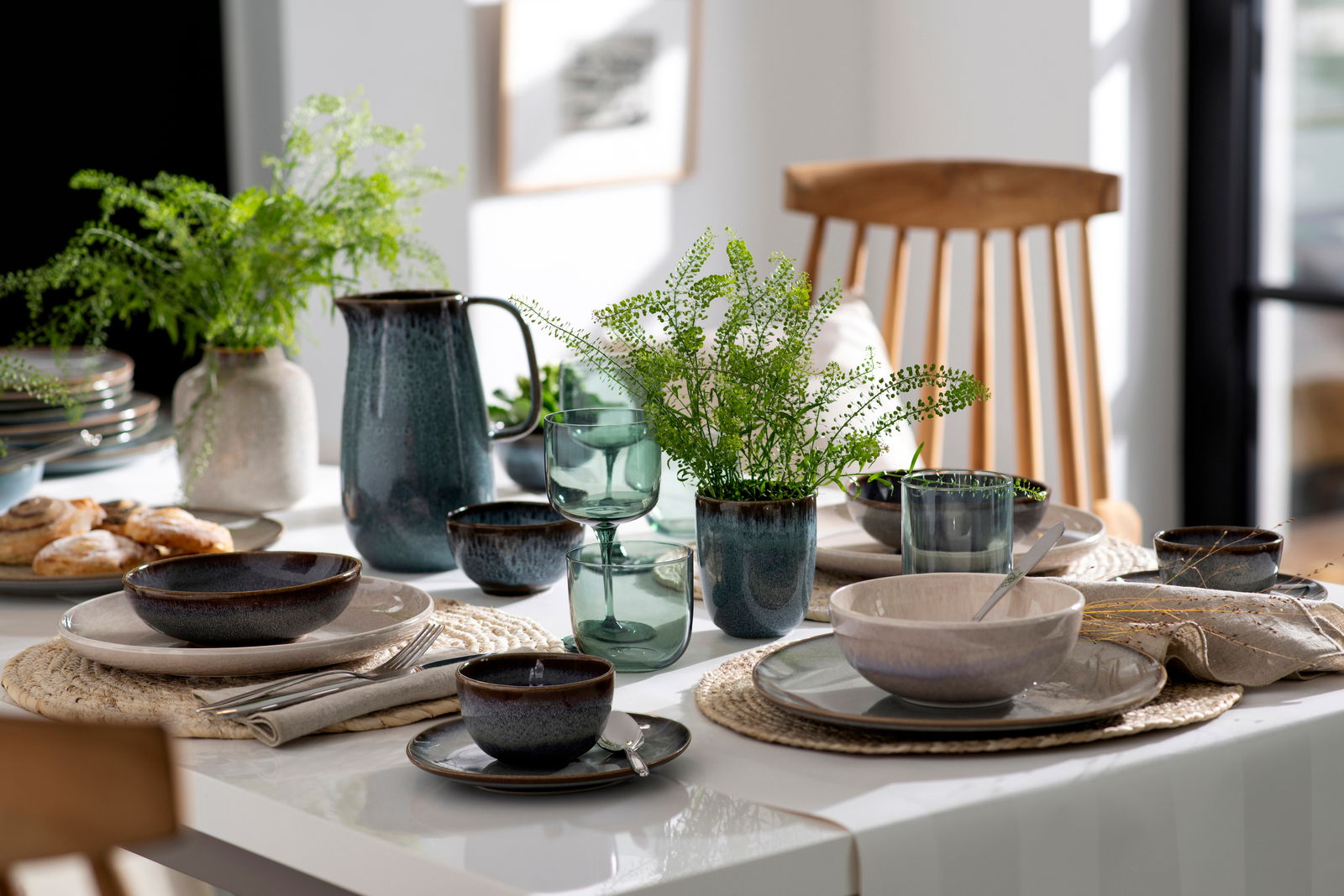 Like by Villeroy & Boch Wasserglas Set 2-tlg. LIKE SAGE Ein stilvoll gedeckter Tisch mit einem Set aus zwei grünen Wassergläsern im Vordergrund, umgeben von Keramikgeschirr und Pflanzen, aus der Perspektive eines seitlichen Blicks.