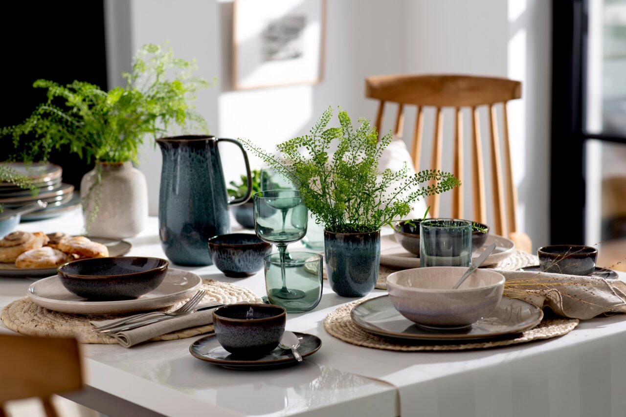 Like by Villeroy & Boch Wasserglas Set 2-tlg. LIKE SAGE Ein stilvoll gedeckter Tisch mit einem Set aus zwei grünen Wassergläsern im Vordergrund, umgeben von Keramikgeschirr und Pflanzen, aus der Perspektive eines seitlichen Blicks.