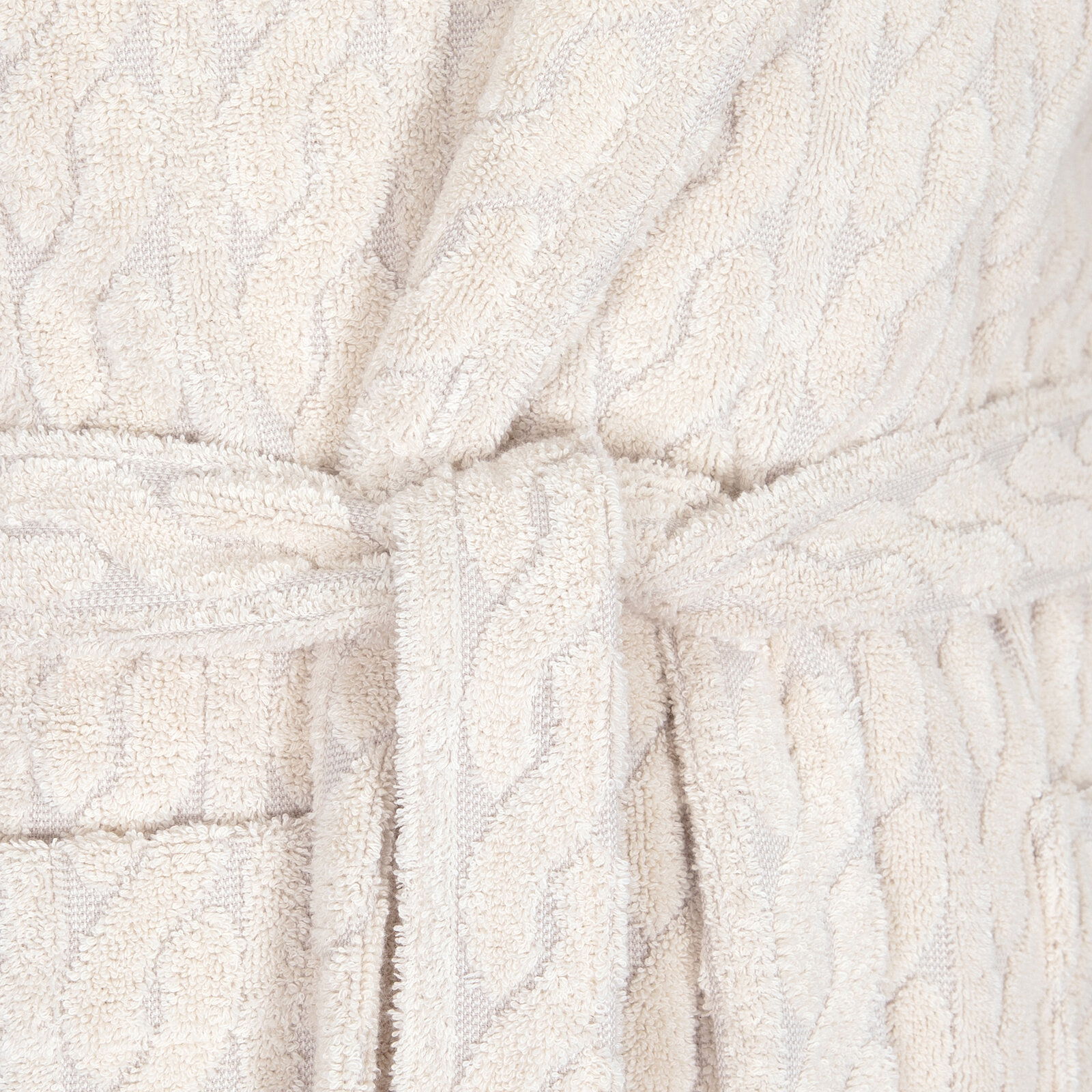 Nahaufnahme eines cremefarbenen Kapuzenmantels mit Gürtel und Strickmuster