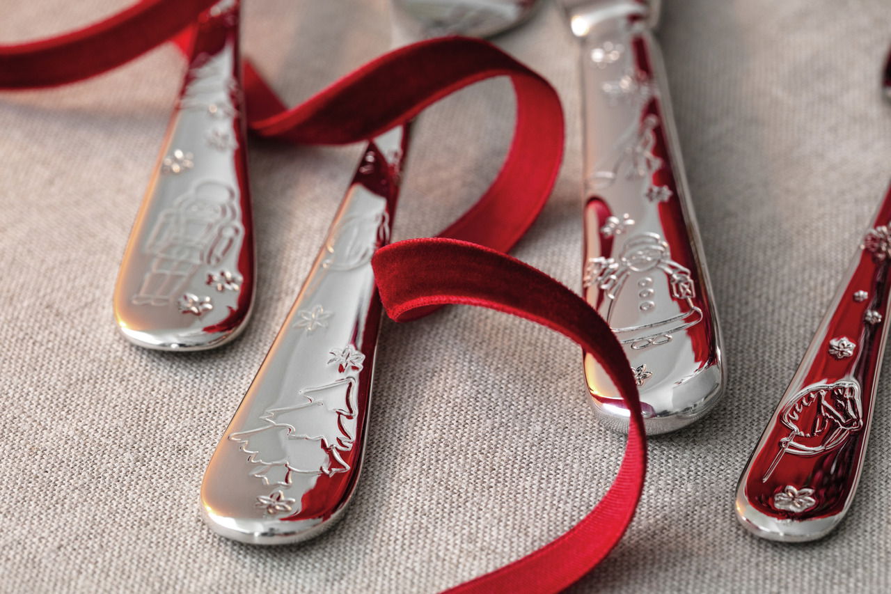 Nahaufnahme von festlichem Tafelbesteck mit weihnachtlichen Motiven und rotem Band, von oben betrachtet.