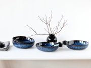 Blau glasierte Keramik-Schalen im Set auf weißem Tisch, dekoriert mit schwarzer Vase und Zweigen, Frontansicht auf Augenhöhe