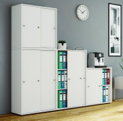 Modulares weißes Büroschranksystem mit Schiebetüren und offenen Regalfächern mit farbigen Ordnern, frontal aus leicht schräger Perspektive aufgenommen
