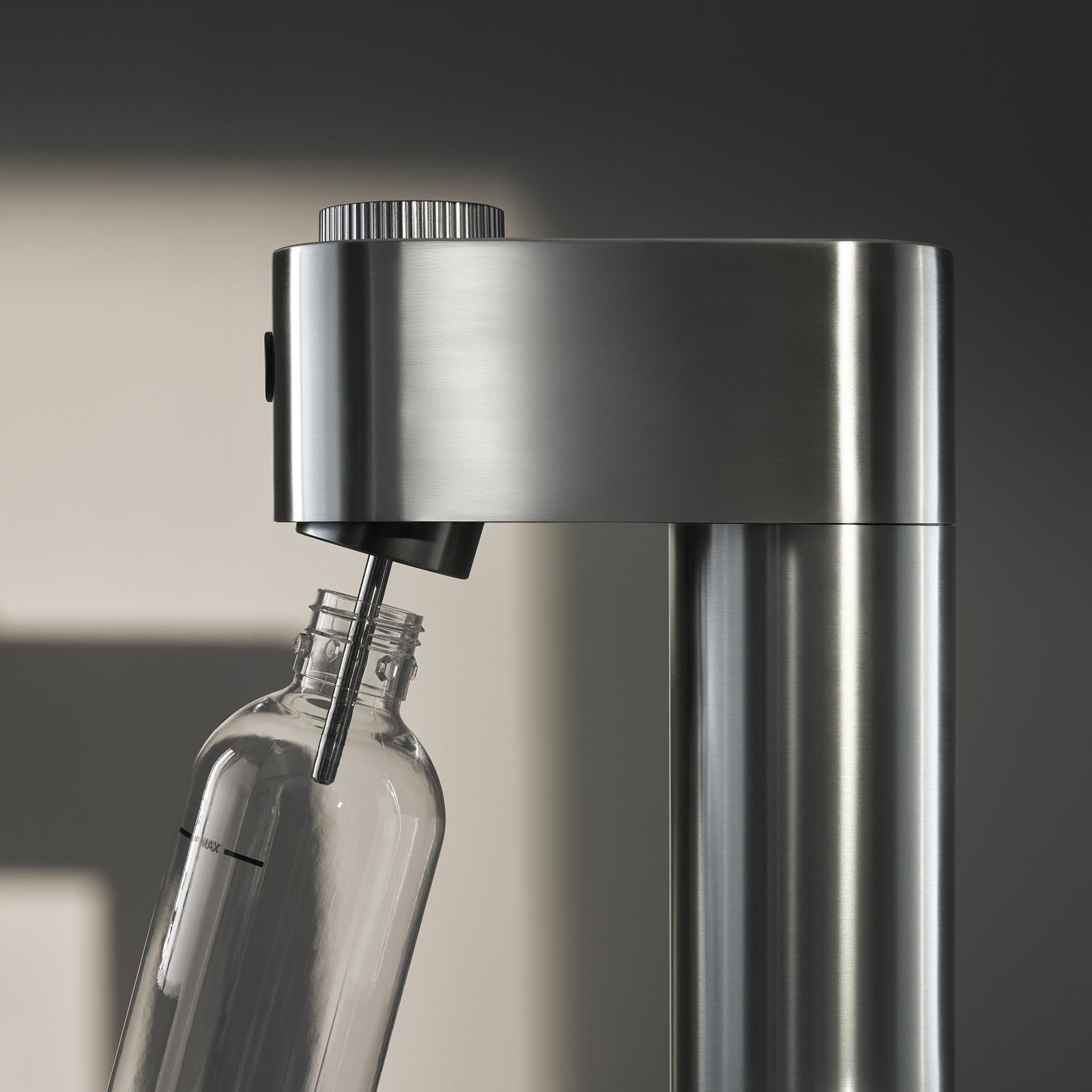 Nahaufnahme eines Wassersprudlers aus Edelstahl mit einer angeschlossenen Glasflasche, seitliche Perspektive.