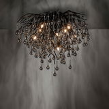 Moderne Deckenleuchte ICICLE mit hängenden, tropfenförmigen Elementen in einer dunklen, eleganten Ausführung. Perspektive von unten, die die komplexe Struktur und das warme Licht betont.
