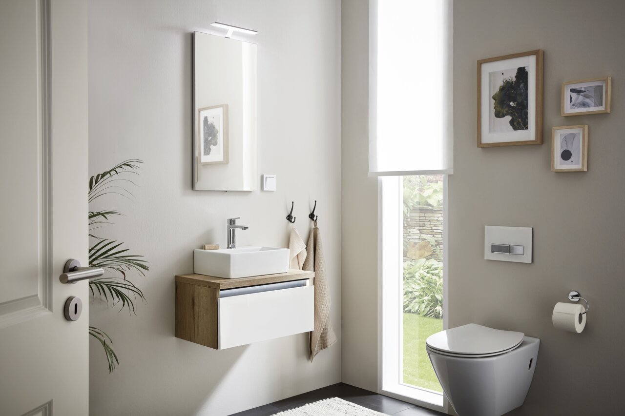Moderne gastenbadkamer met hangende wastafel, spiegel met verlichting en toilet, zijaanzicht.