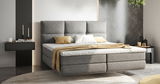 Modernes Boxspringbett in grauem Stoff mit hohem Kopfteil, dekoriert mit Kissen und Decke, seitliche Perspektive