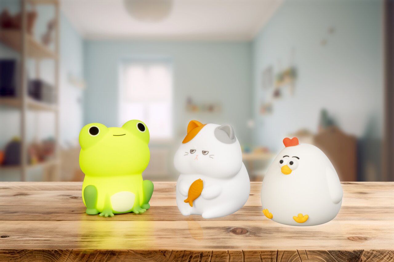 Vorderansicht von drei Akku-Nachtlichtern in Form eines leuchtenden Frosches, einer Katze mit Fisch und eines Huhns auf einem Holztisch in einem Kinderzimmer.