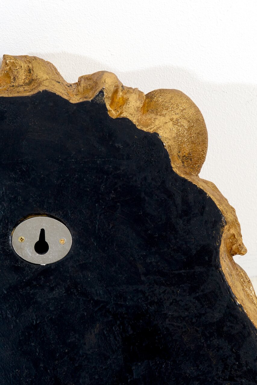 Nahaufnahme einer Wandleuchte mit unregelmäßiger goldener Kante und schwarzer Oberfläche, Rückansicht mit Schlüsselloch.