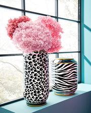 Vase mit Leopardenmuster, gefüllt mit rosa und pinken Blumen, auf einer Fensterbank stehend, seitliche Perspektive