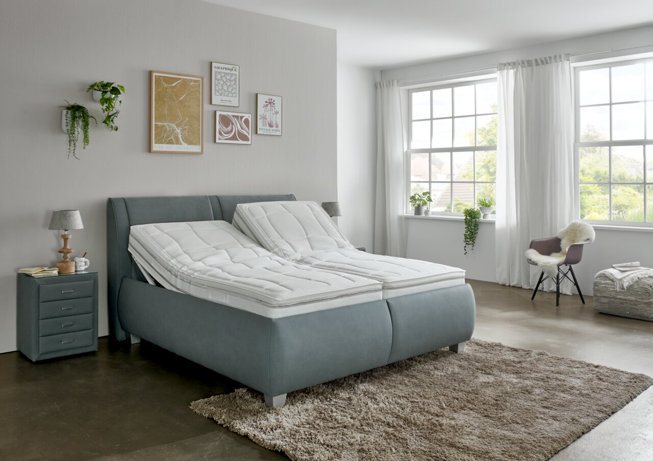 Modernes Polsterbett in einem hellen Schlafzimmer, seitliche Perspektive, mit verstellbaren Matratzen und stilvoller Dekoration.