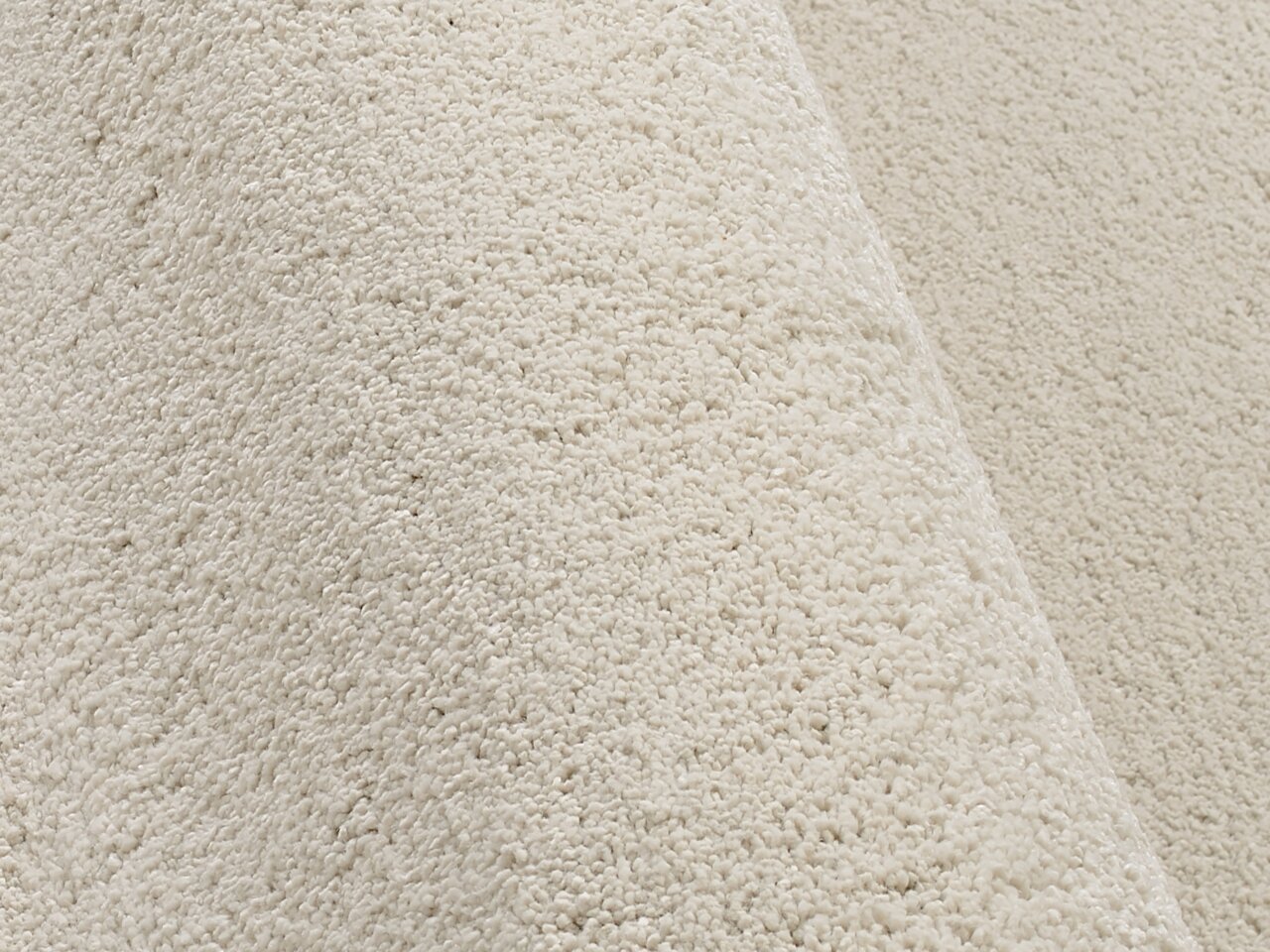 Nahaufnahme eines cremefarbenen Uni-Teppichs mit weicher, flauschiger Textur, seitliche Perspektive