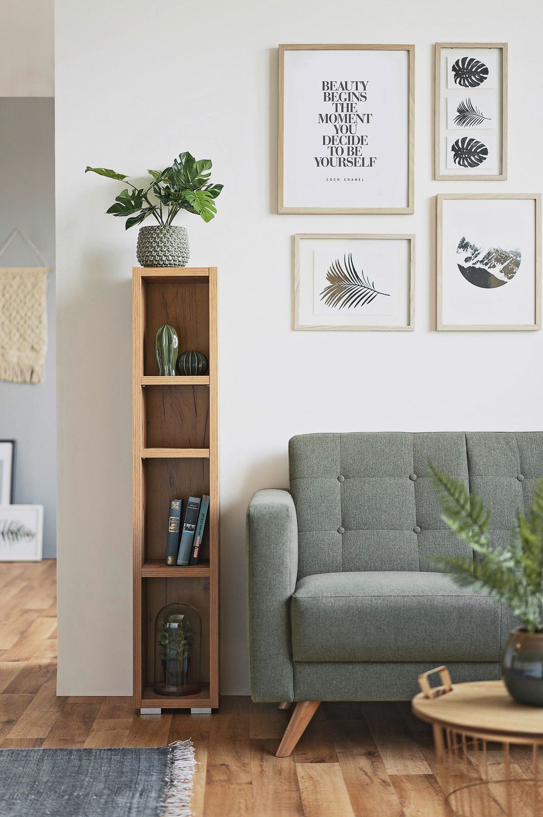 Schmales, hohes Regal aus Holz mit mehreren Fächern, dekoriert mit Pflanzen und Büchern, neben einem grünen Sofa in einem modernen Wohnzimmer. Frontalansicht.