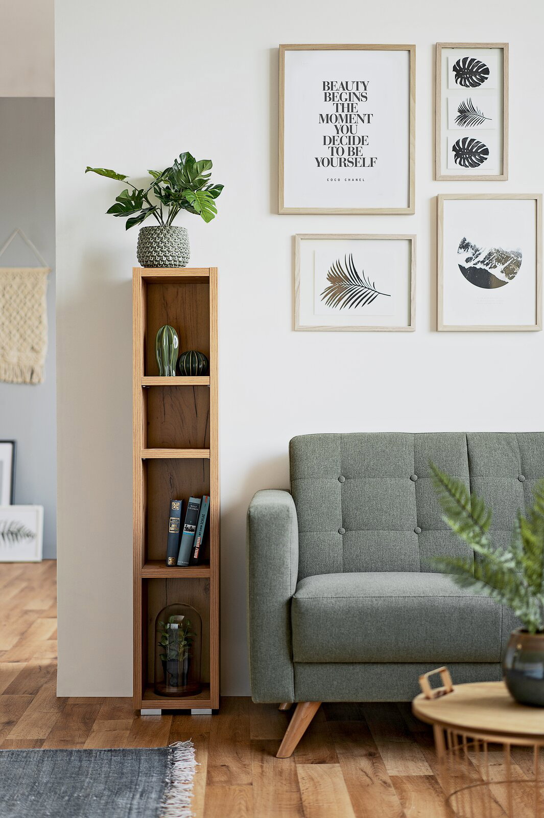 Schmales, hohes Regal aus Holz mit mehreren Fächern, dekoriert mit Pflanzen und Büchern, neben einem grünen Sofa in einem modernen Wohnzimmer. Frontalansicht.
