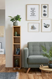 Een smalle, hoge houten kast met meerdere vakken, versierd met planten en boeken, naast een groene bank in een moderne woonkamer. Vooraanzicht.