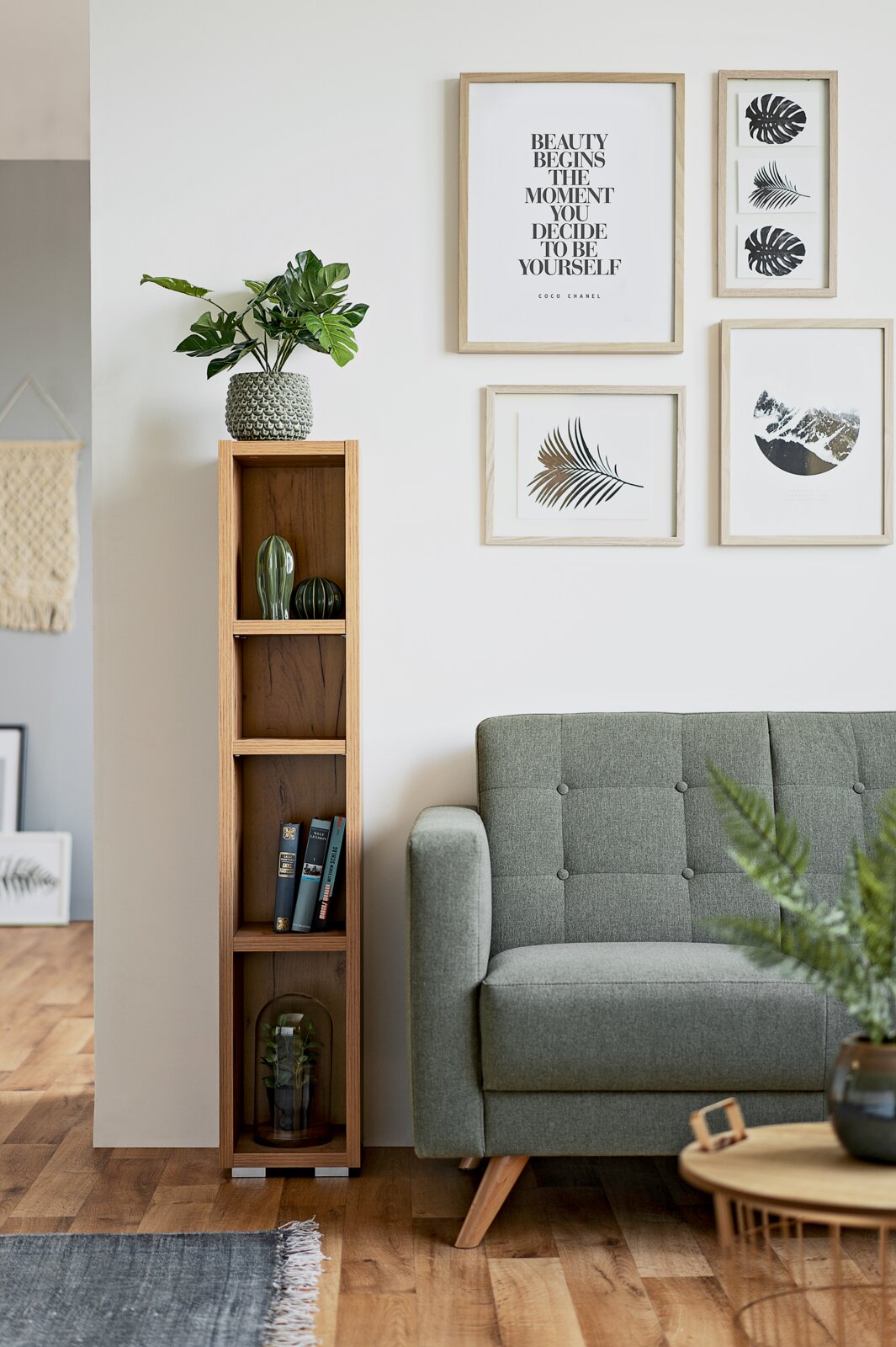 Een smalle, hoge houten kast met meerdere vakken, versierd met planten en boeken, naast een groene bank in een moderne woonkamer. Vooraanzicht.