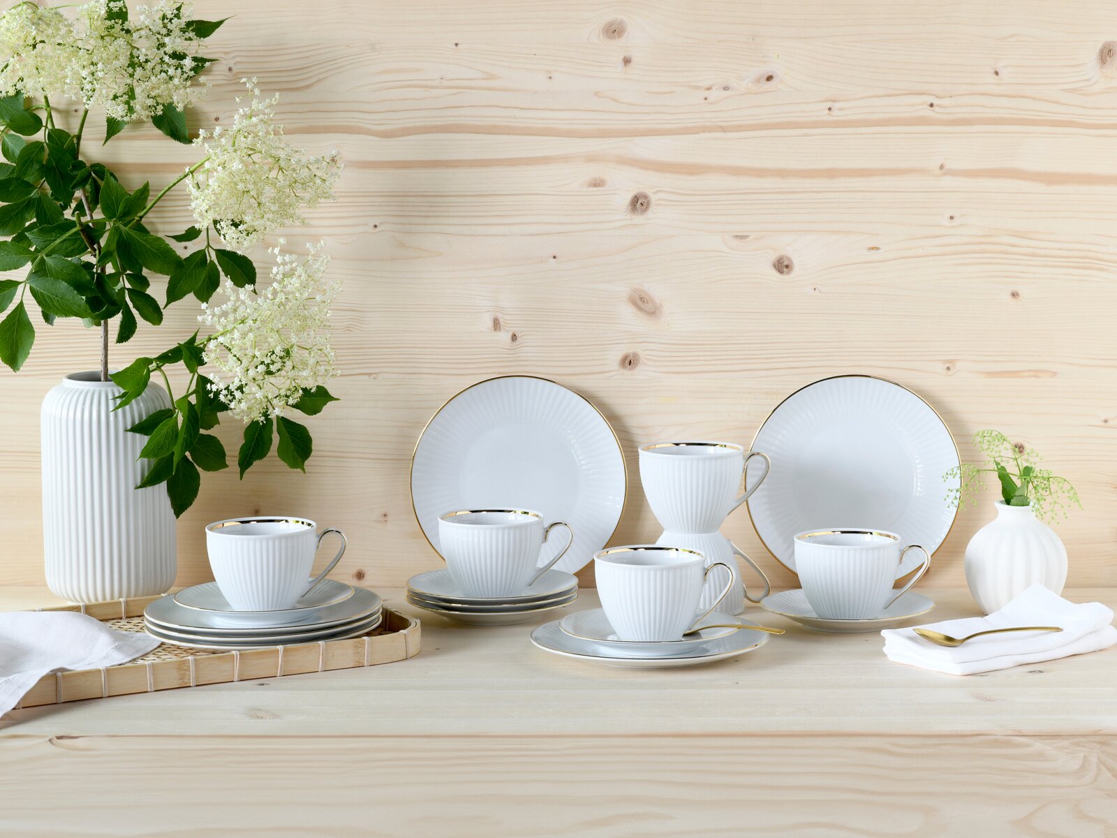 Creatable Kaffeeservice 18-tlg VALENCIA Weißes geriffeltes Porzellan-Kaffeegeschirr mit goldfarbenem Rand (Tassen, Untertassen und Teller) dekorativ auf hellem Holztisch arrangiert, Perspektive: frontal/leicht von vorne.