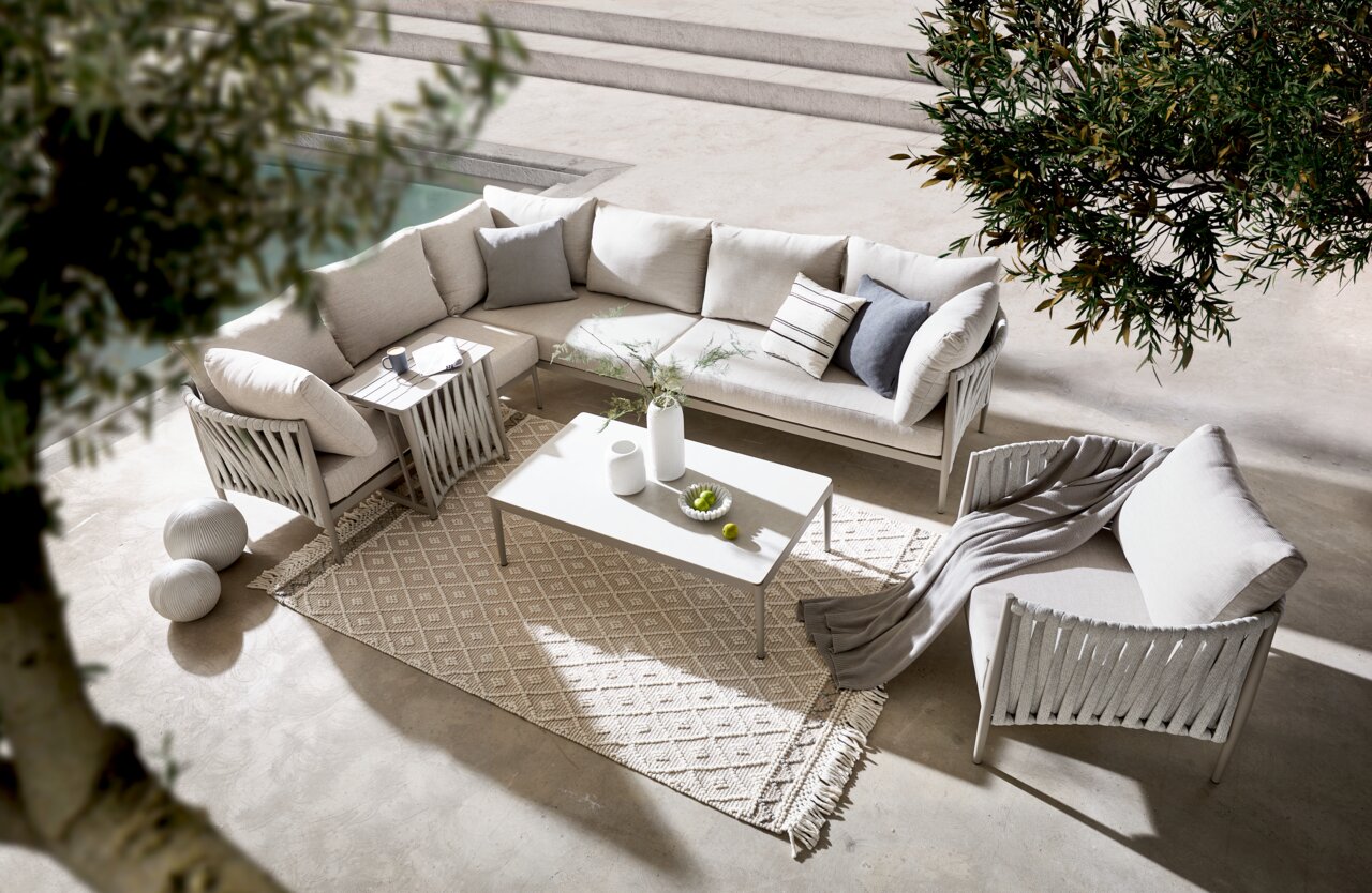 Amatio Loungeset VENERONA Loungegarnitur in einer eleganten, modernen Umgebung, von oben fotografiert. Die Garnitur besteht aus einem Ecksofa mit hellen Kissen, einem Couchtisch und einem Teppich, umgeben von Pflanzen.