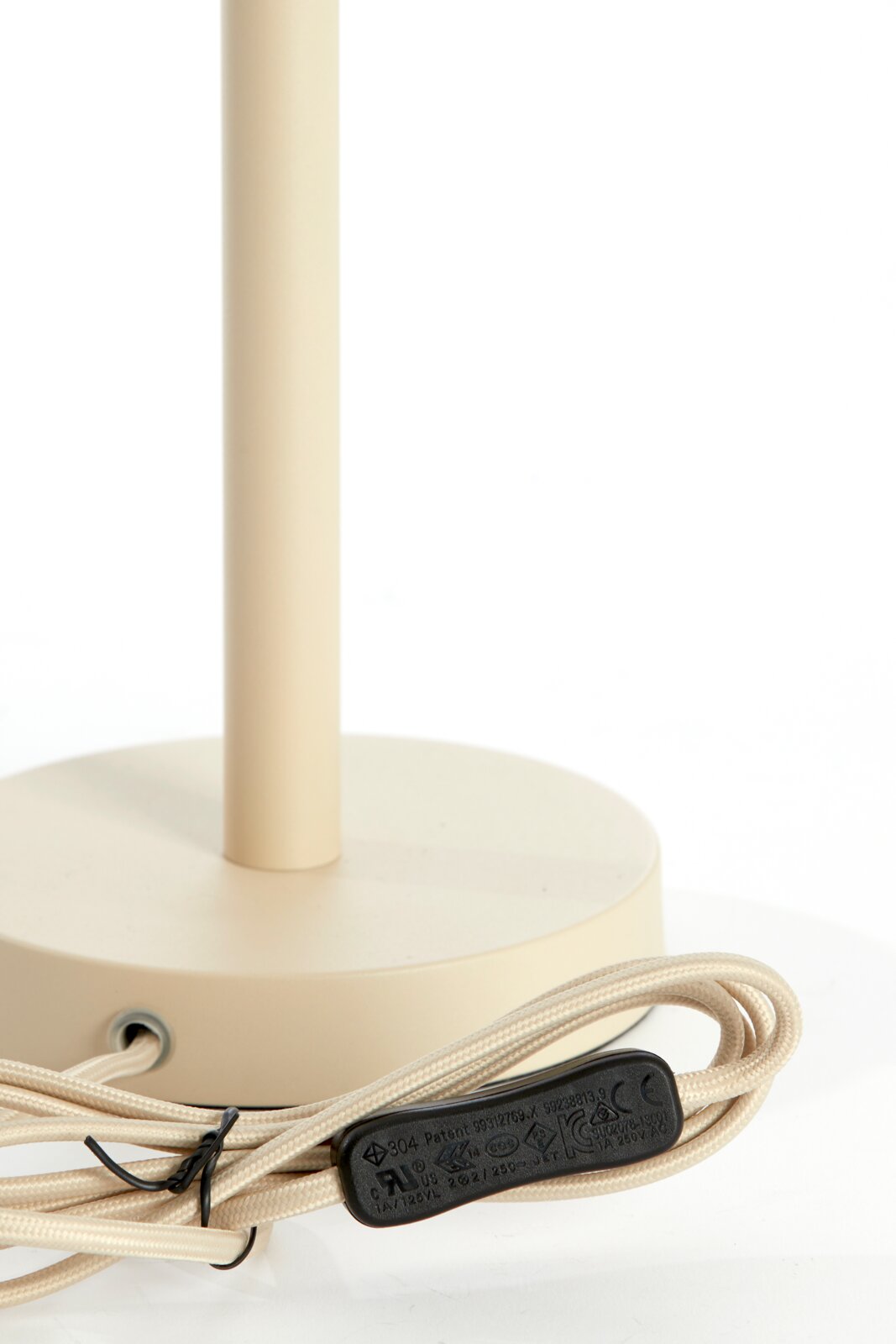 Nahaufnahme eines beigen Lampenfußes mit rundem Sockel und beige ummanteltem Kabel, seitliche Perspektive.