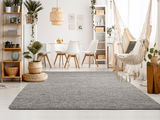 Grauer Handweb Teppich in einem modernen Wohnzimmer mit Pflanzen, Hängesessel und Esstisch, aus der Perspektive des Bodenbereichs fotografiert.