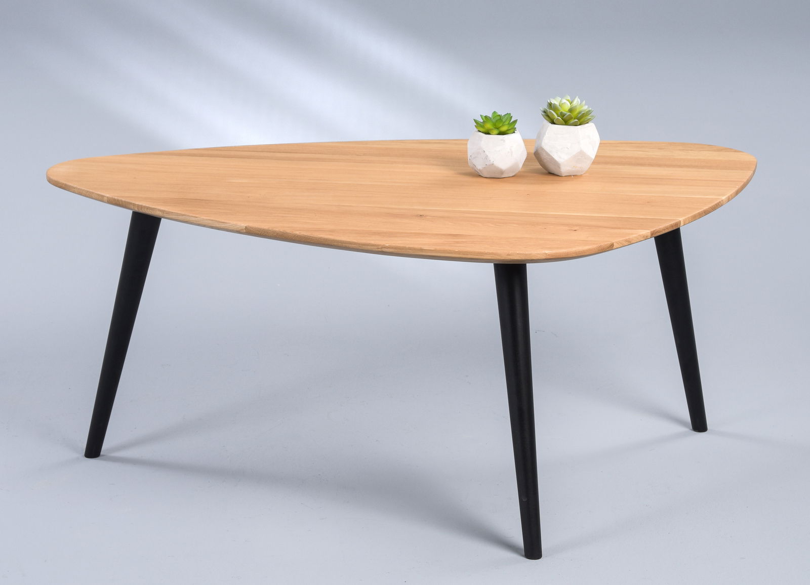 Moderner Couchtisch mit dreieckiger Holzplatte und schwarzen Beinen, seitliche Perspektive