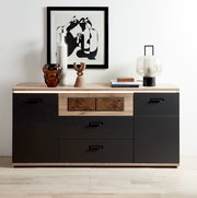 Moderne Sideboard-Kommode in Schwarz mit Holzplatte und mittlerer Holz-Schubladenfront, dekoriert mit Vase, Skulptur, Büchern und Tischlampe; frontale Perspektive auf das Möbel vor weißer Wand.