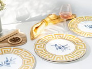 Sommerlich gedeckter Tisch mit weißem Geschirr: Teller mit gelbem Mäander-Rand und blauem Olivenzweig-Motiv, gelbe Stoffserviette mit Ring, Weinglas mit Rosé sowie Holzbrett mit Gewürzen – Perspektive: leicht von oben, schräger Blickwinkel.