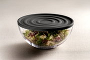 Transparente Schale mit schwarzem Deckel, gefüllt mit frischem Salat, seitliche Perspektive