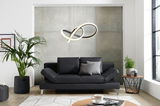 Schwarzes Querschläfer-Sofa in modernem Wohnzimmer, frontal fotografiert, mit Pflanzen und Couchtisch.