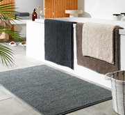 Badteppich in Grau, 70x120 cm, auf Badezimmerboden, mit weiteren Handtüchern an der Badewanne, seitliche Perspektive