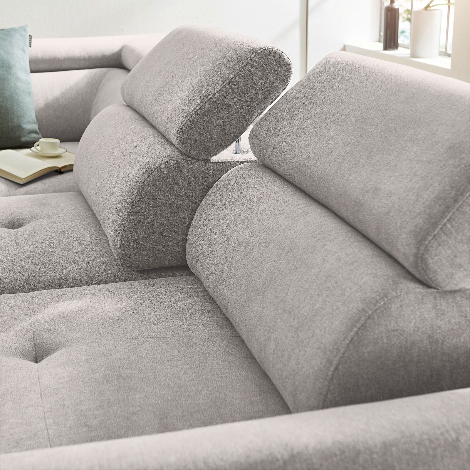 Nahaufnahme eines grauen Ecksofas mit verstellbaren Kopfstützen, weicher Polsterung und einem modernen Design. Perspektive von der Seite.