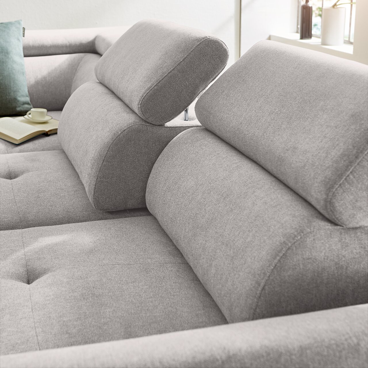 Nahaufnahme eines grauen Ecksofas mit verstellbaren Kopfstützen, weicher Polsterung und einem modernen Design. Perspektive von der Seite.