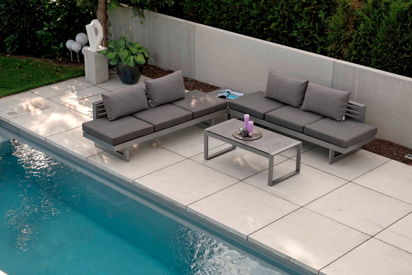 Moderne Lounge-Möbel auf einer Terrasse neben einem Pool, aus der Vogelperspektive fotografiert.