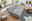 Graues Funktionssofa in einem modernen Wohnzimmer, von oben betrachtet, mit ausgezogener Liegefläche, umgeben von Pflanzen, einem Kamin und einem Couchtisch.