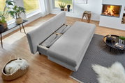 Graues Funktionssofa in einem modernen Wohnzimmer, von oben betrachtet, mit ausgezogener Liegefläche, umgeben von Pflanzen, einem Kamin und einem Couchtisch.