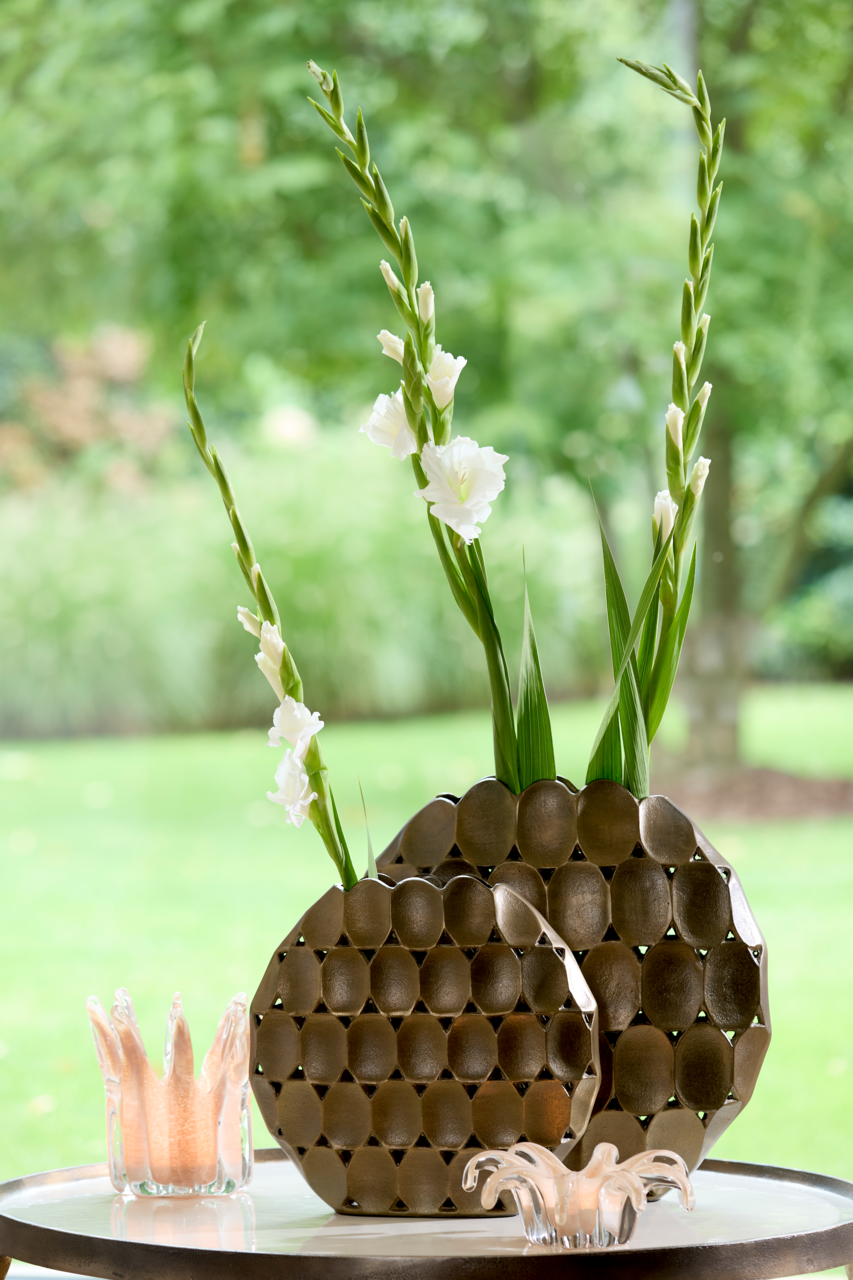 Zwei dekorative Vasen mit wabenartigem Muster, gefüllt mit weißen Blumen, auf einem Tisch im Freien, seitliche Perspektive.