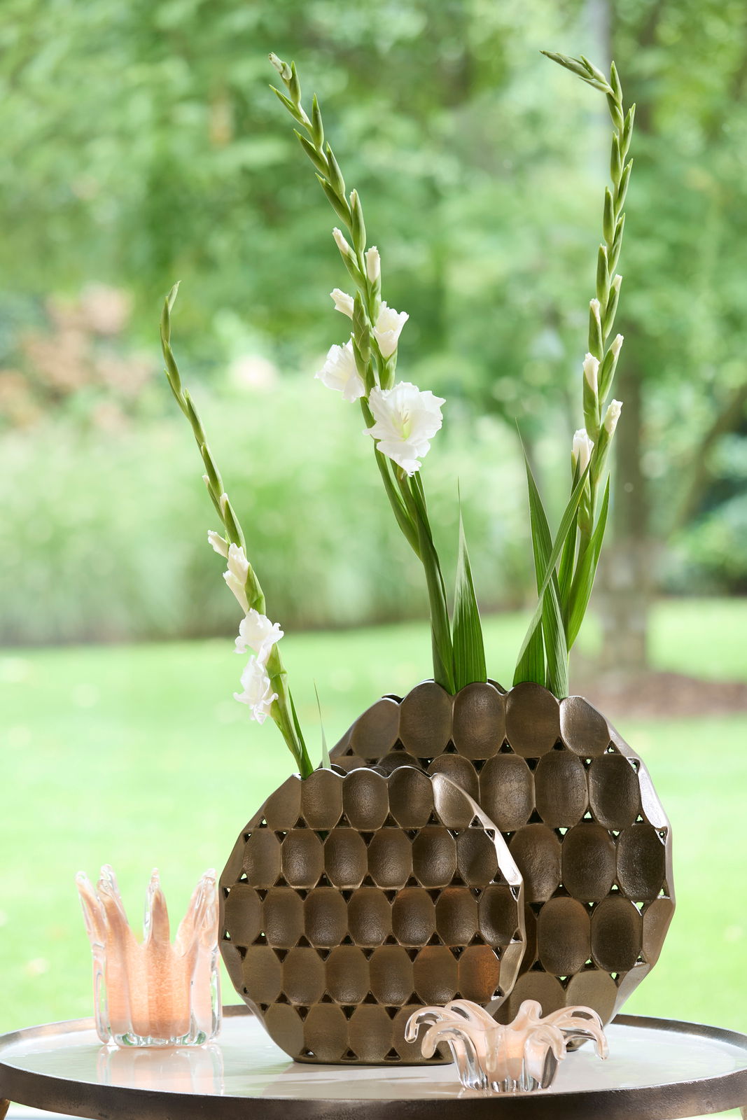 Light&Living Vase ORLAN 33cm Zwei dekorative Vasen mit wabenartigem Muster, gefüllt mit weißen Blumen, auf einem Tisch im Freien, seitliche Perspektive.