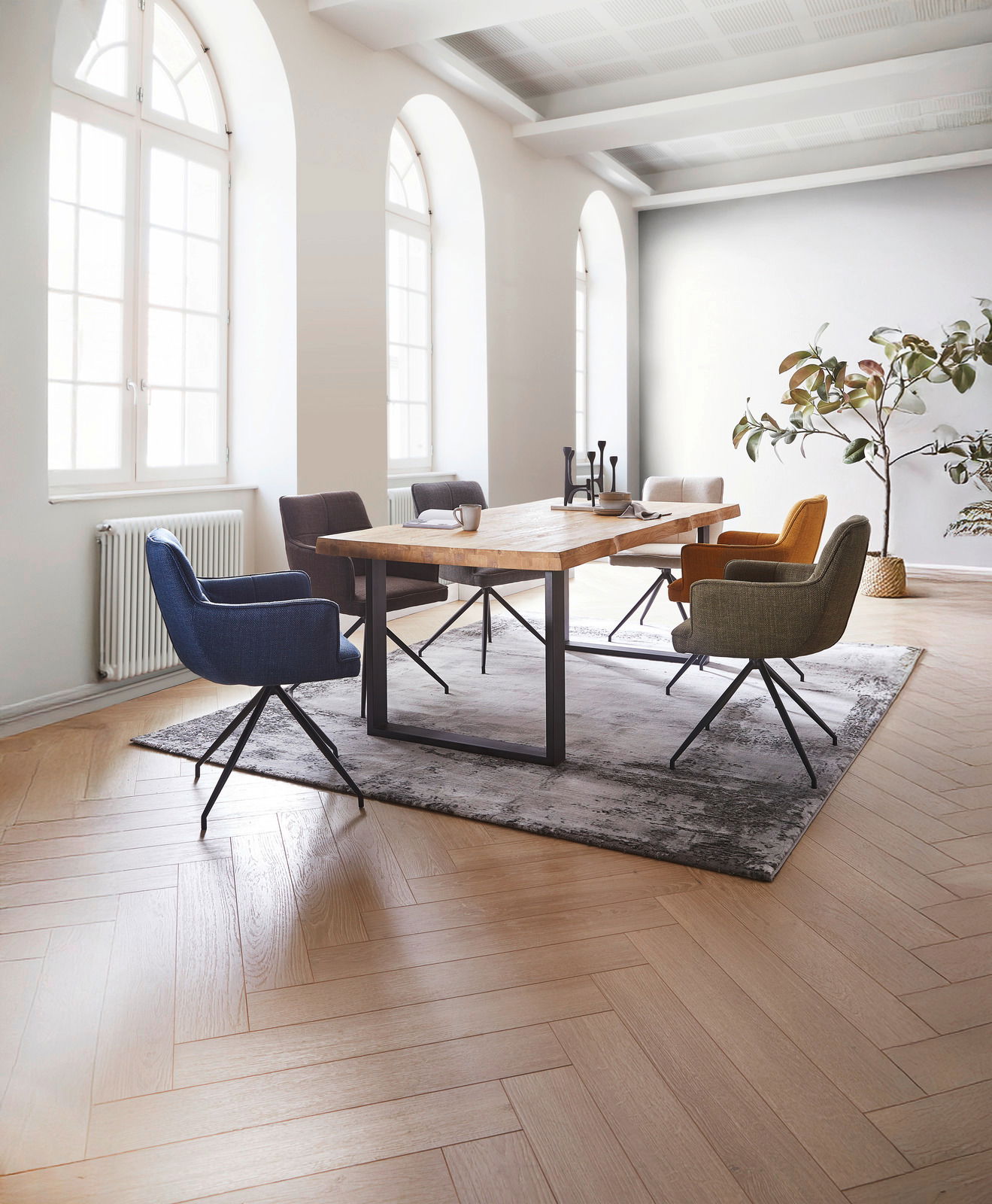 Esszimmer mit einem großen Holztisch und sechs farbigen Armlehnstühlen, seitliche Perspektive