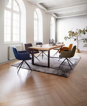 Esszimmer mit einem großen Holztisch und sechs farbigen Armlehnstühlen, seitliche Perspektive