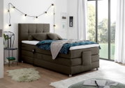Gemütliches Boxspringbett in modernem Schlafzimmer mit Lichterkette und großem Fenster, seitliche Perspektive