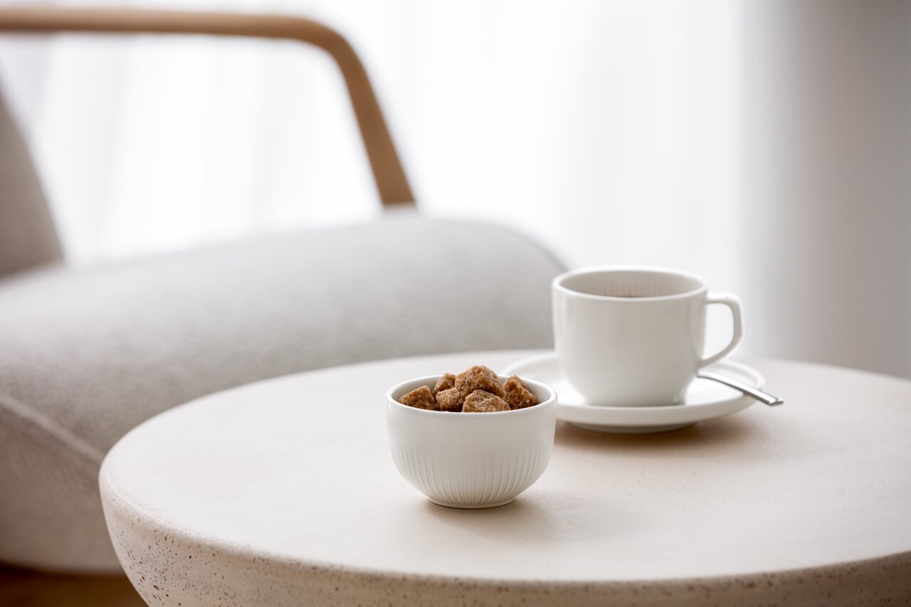 Weiße Dipschale Afina 90ml mit Zuckerwürfeln auf einem runden Tisch, im Hintergrund eine Tasse mit Untertasse und Löffel, seitliche Perspektive