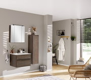 Moderner Badezimmer-Mittelschrank in dunkler Holzoptik, rechts an der Wand montiert, mit dekorativen Elementen und Spiegel im Vordergrund, seitliche Perspektive.