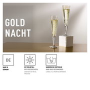 Zwei elegante Champagnergläser mit goldenen Verzierungen, eines auf einem weißen Sockel, auf einem Tisch in seitlicher Perspektive.