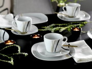 Modernes weißes Porzellan-Kaffeeservice mit Tassen, Untertassen und Tellern mit schwarzen und goldenen Linien, dekoriert mit Kerzen und Blumen auf dunklem Tisch, Perspektive: leicht erhöhte schräge Ansicht von vorne