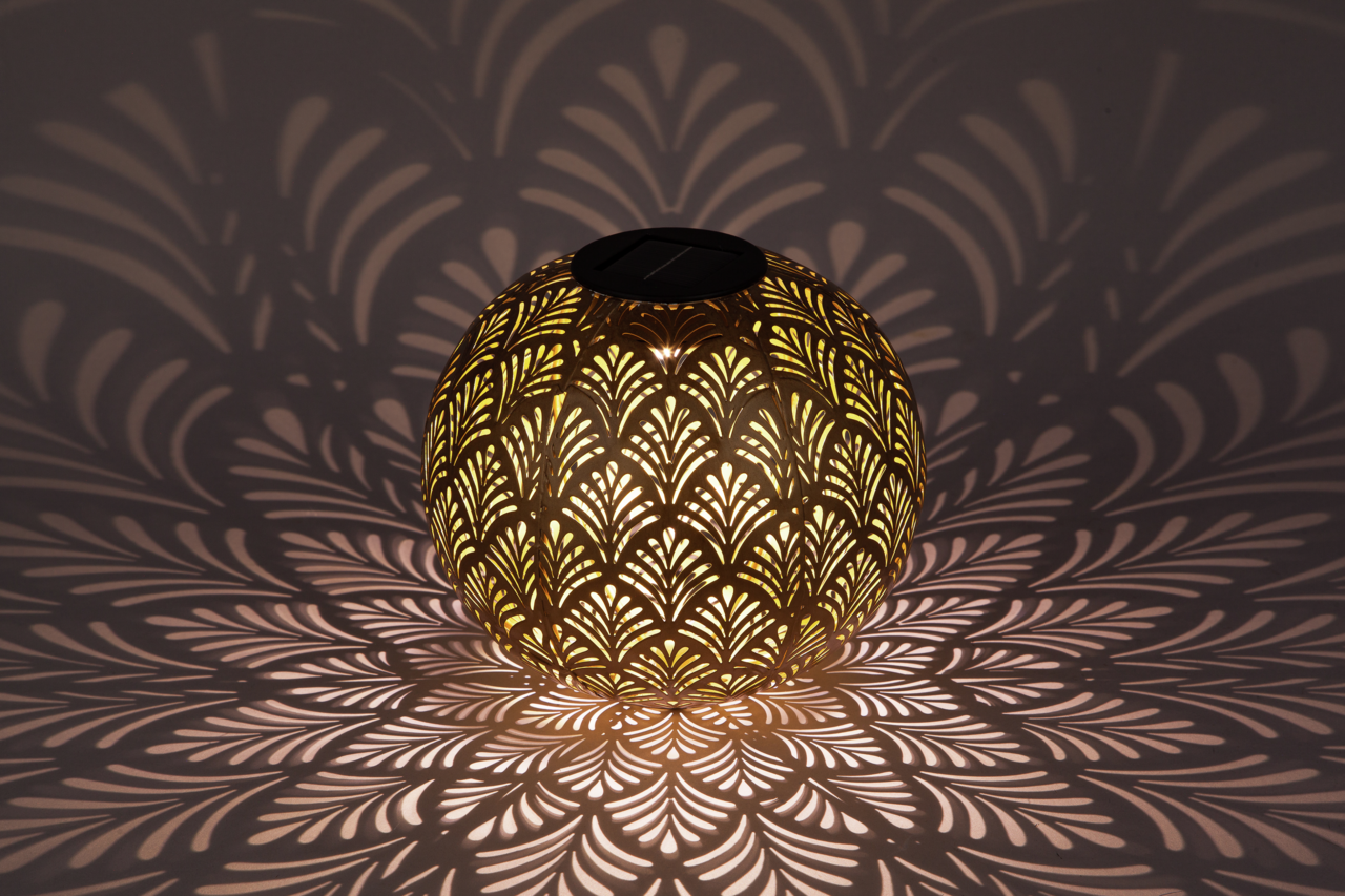 Kugelförmige Solarleuchte mit dekorativem Muster, das ein faszinierendes Licht- und Schattenspiel auf die Umgebung wirft, seitliche Perspektive.