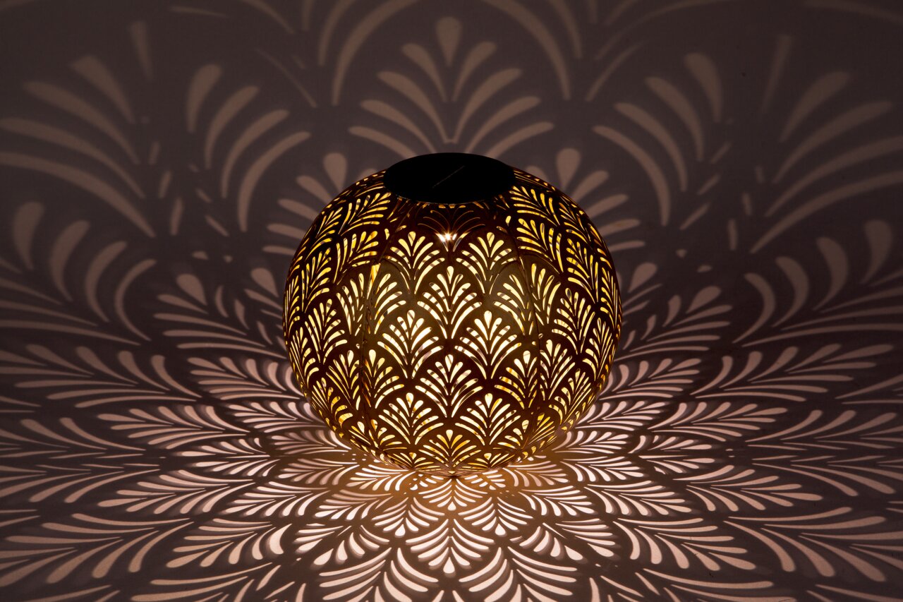 Kugelförmige Solarleuchte mit dekorativem Muster, das ein faszinierendes Licht- und Schattenspiel auf die Umgebung wirft, seitliche Perspektive.